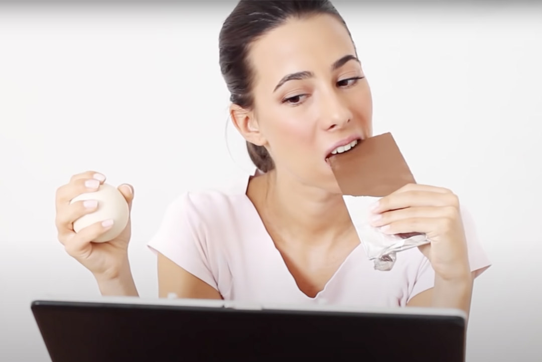 a person eating chocolate and squeezing stress ball at computer